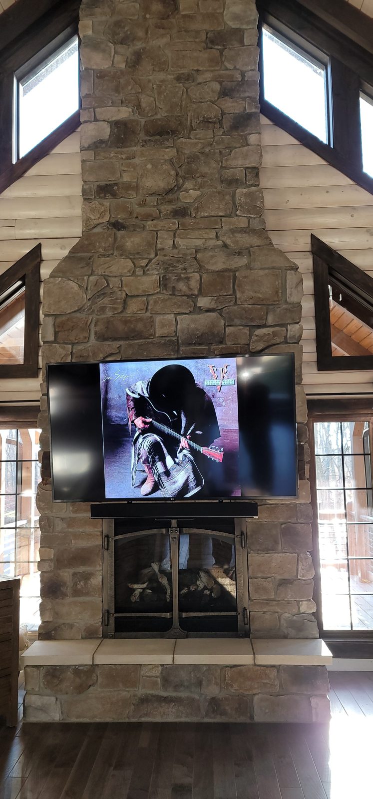 Television installed on a Mantle Mount over a stone fireplace by Noble A-V