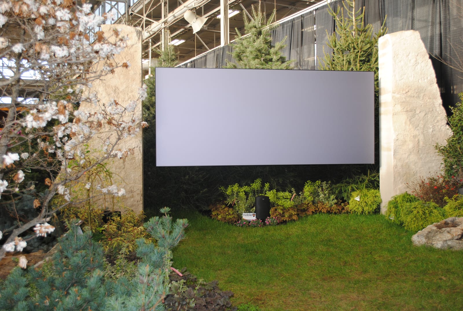 Outdoor television display integrated into a landscape installation, evergreen plantings to either side