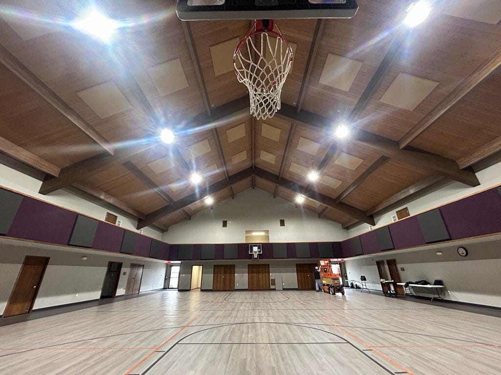 Vaulted-ceiling worship gymnasium with installed acoustic absorber panels and basketball goal