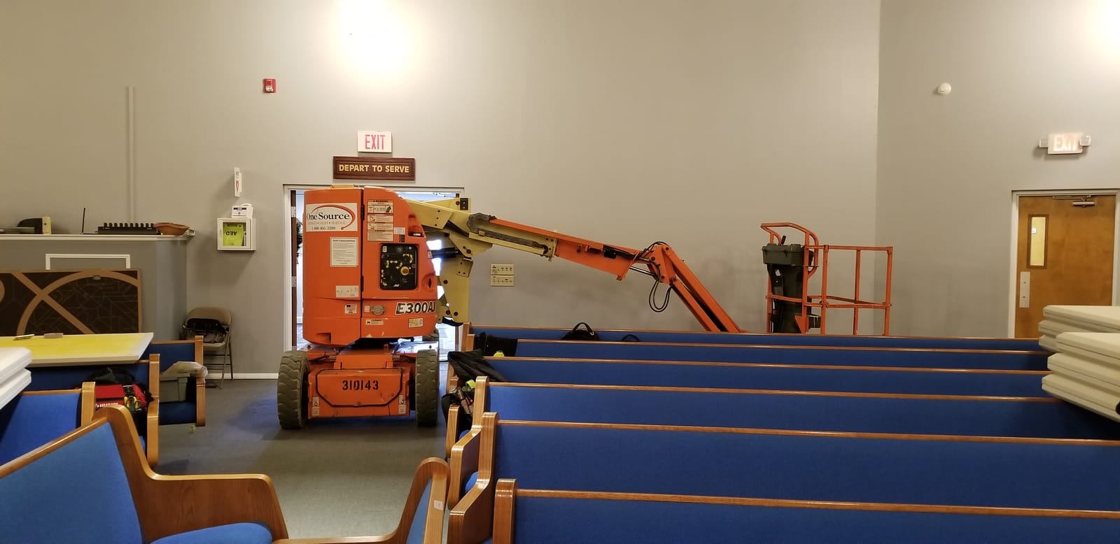 Noble A-V technician working on high-mounted speaker and lighting from a scissor lift inside a sanctuary